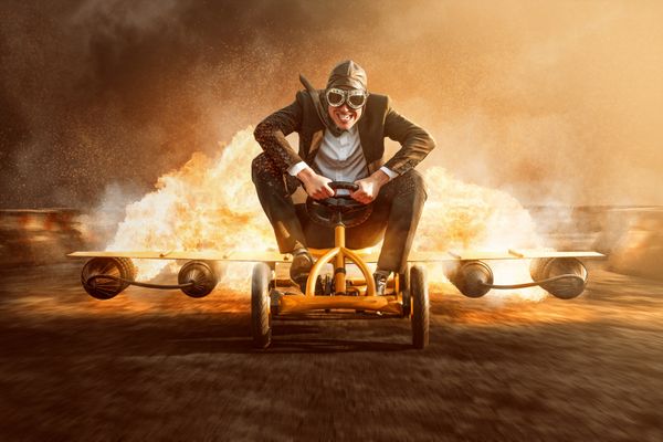 Man on tricycle that has plane wings with flames behind him
